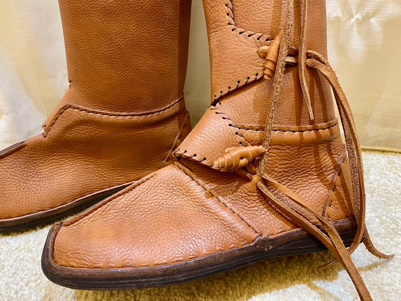 Pair of brown leather boots with decorative laces on a light background