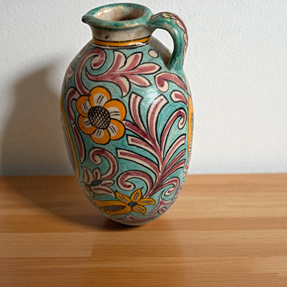 Decorated ceramic pitcher with handle, floral pattern, set on wooden surface.
