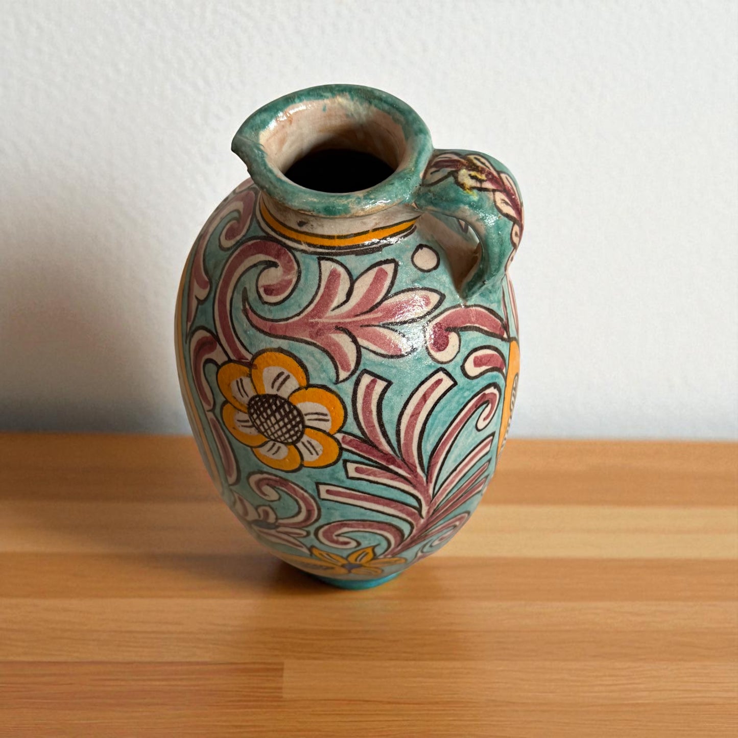 Ornate, colorful ceramic pitcher on wooden surface.