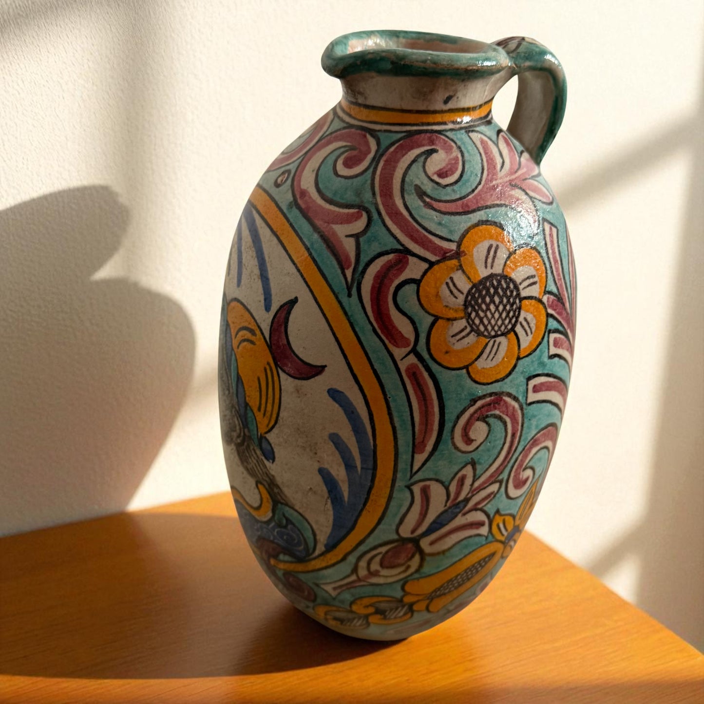 Hand-painted ceramic pitcher with floral and scroll designs.