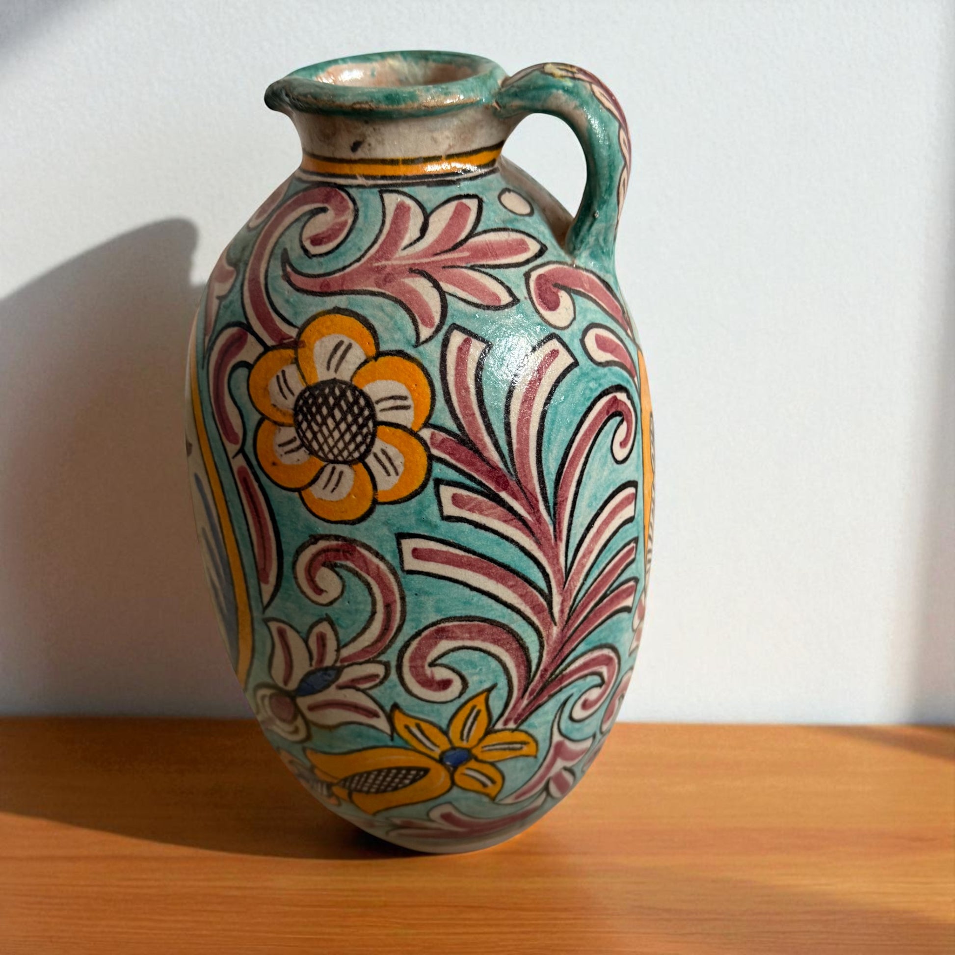Decorated ceramic pitcher with handle on a wooden surface.