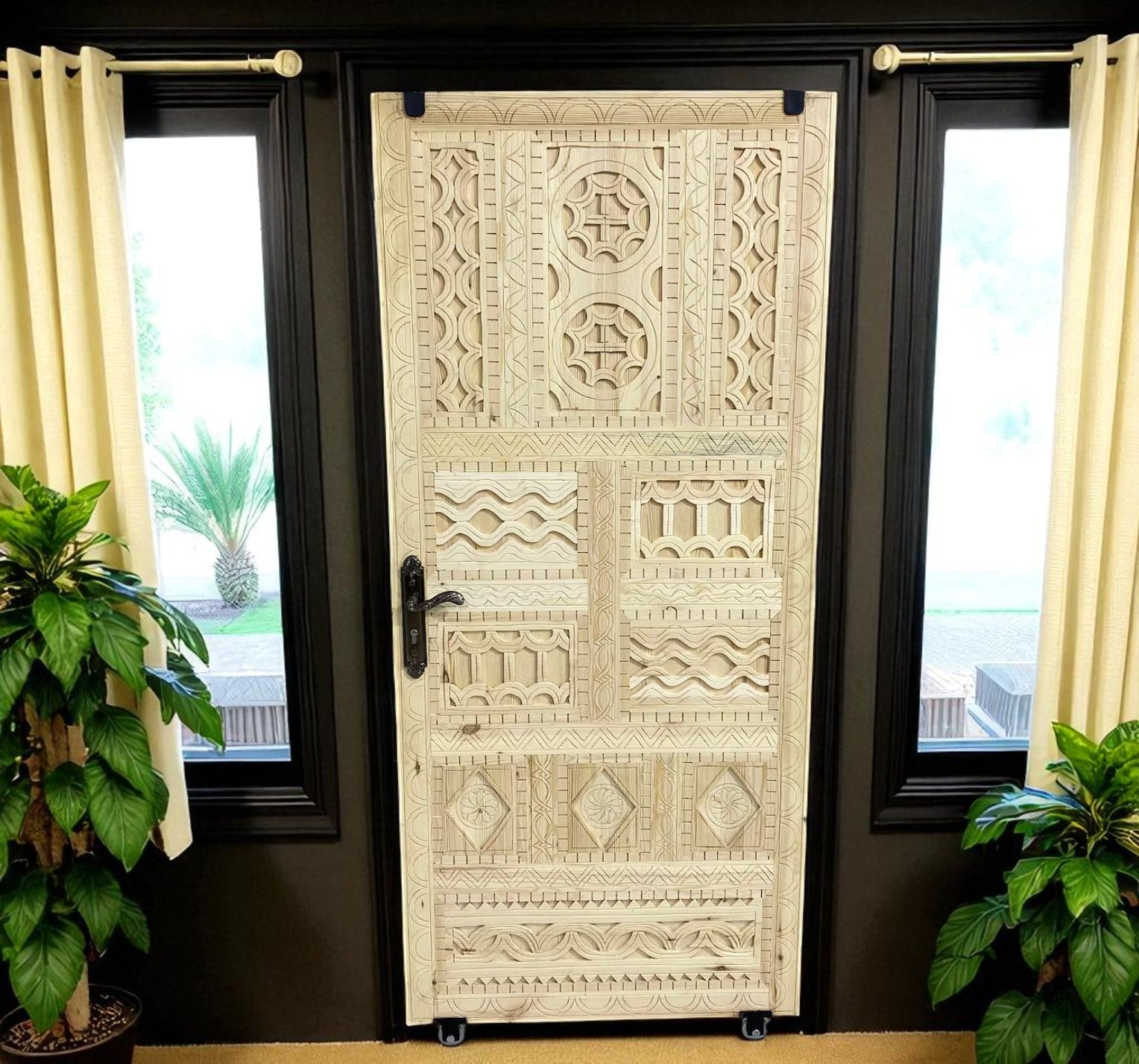 Ornate carved wooden door with black metal hardware, flanked by windows with beige curtains and plants.