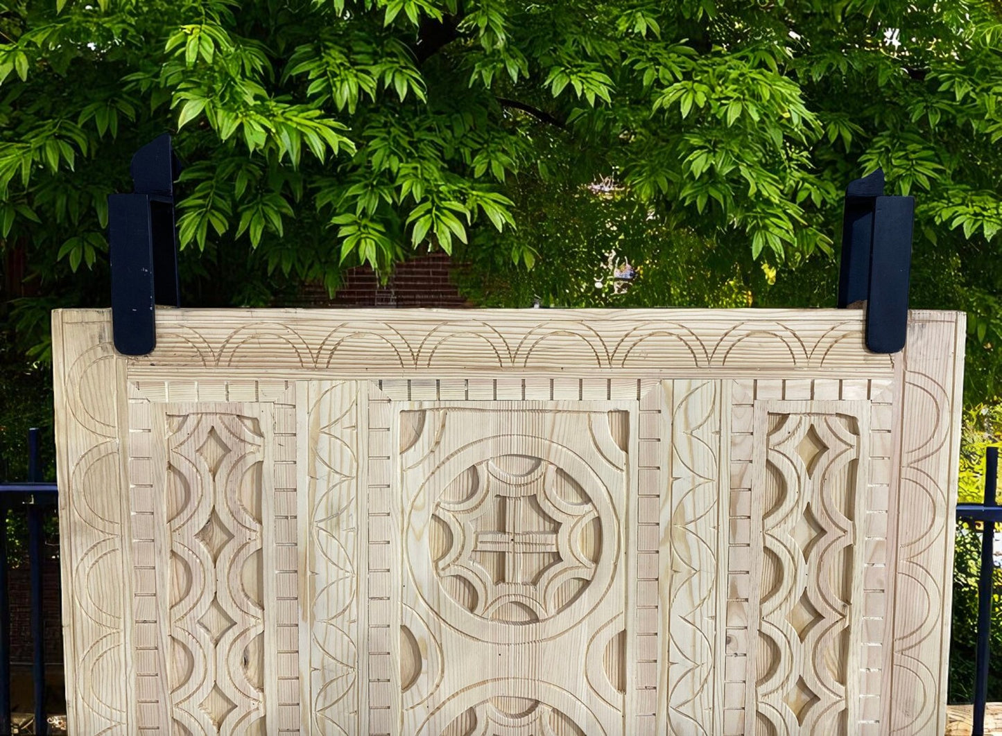 Carved wooden headboard with dark metal supports, green foliage backdrop.