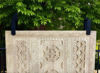 Carved wooden headboard with dark metal supports, green foliage backdrop.