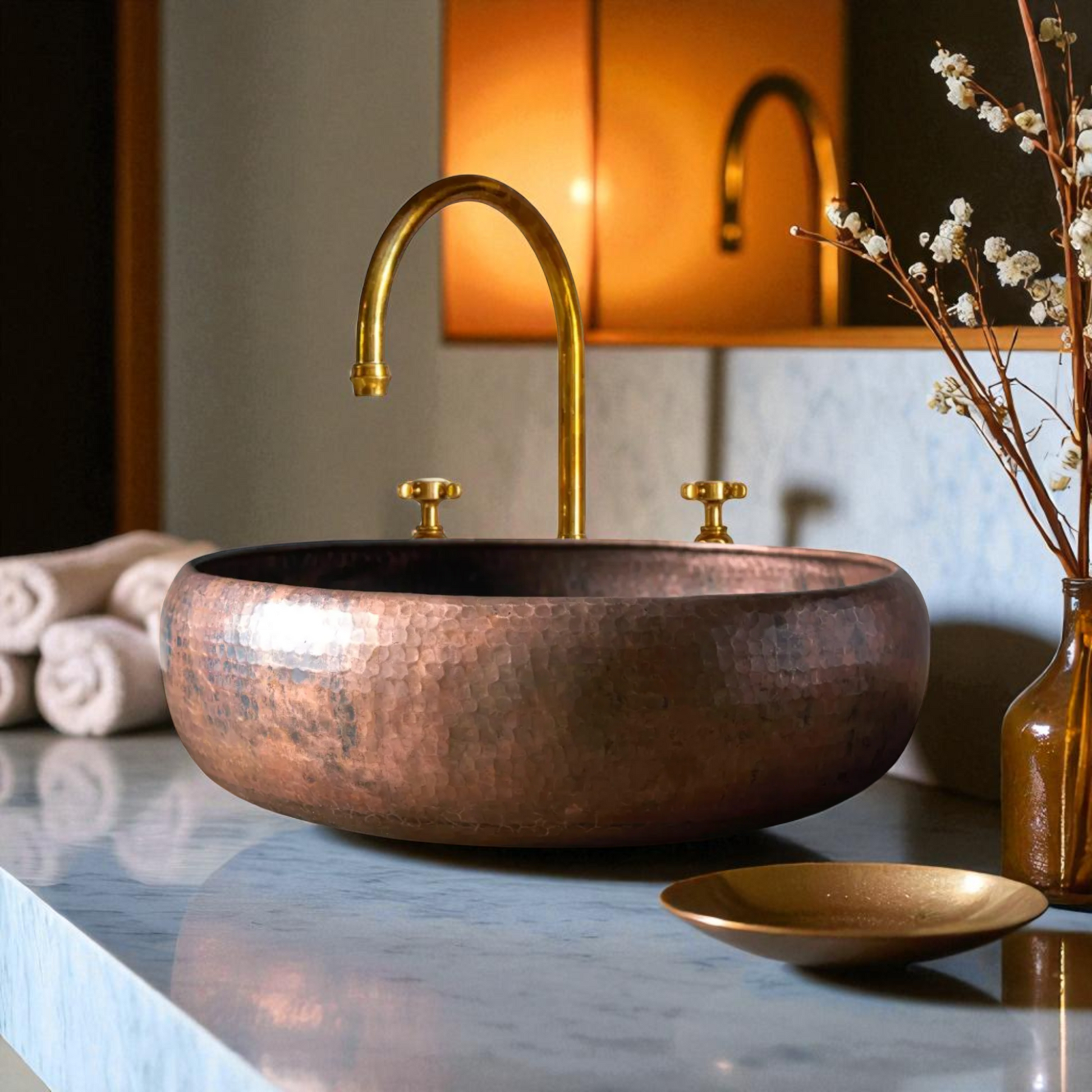 Copper sink with brass faucet, towel, and flowers on marble countertop.