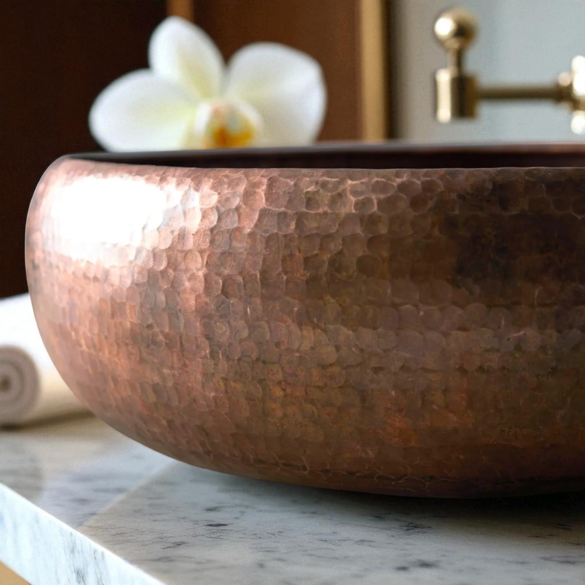 Close-up of a hammered copper vessel sink on a marble countertop, with a white orchid and gold faucet in the background.