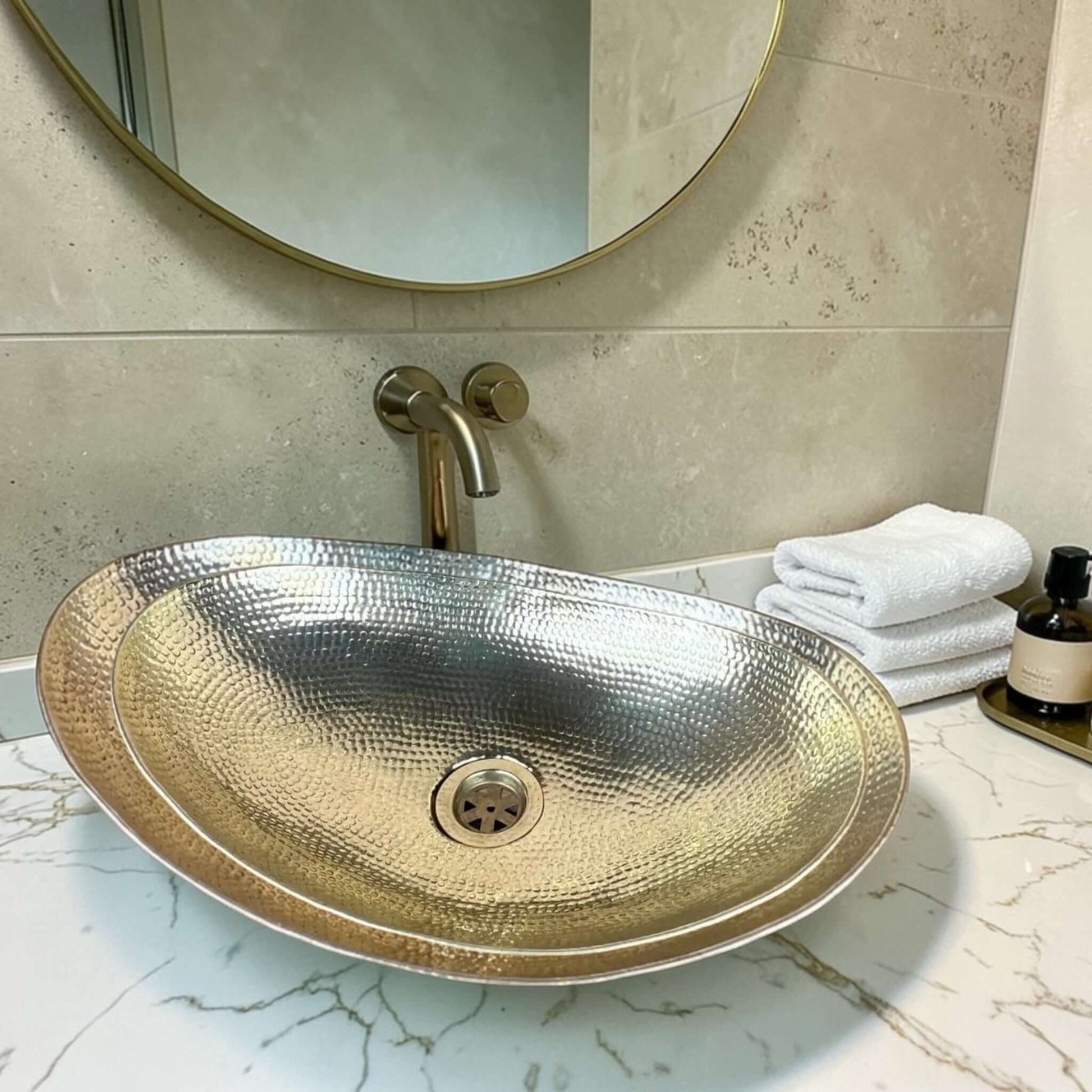 Hammered brass bathroom vessel sink elegantly displayed on a marble countertop with a round mirror.