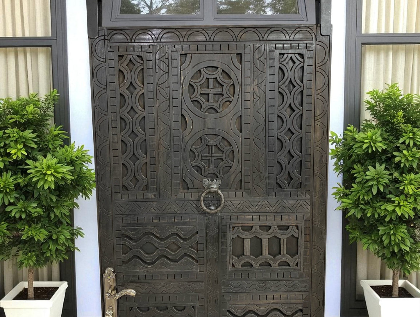 Ornate wooden door with geometric carvings and a ring knocker, flanked by potted trees.