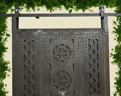Elaborately carved, dark wood barn door with iron sliding track and hardware.
