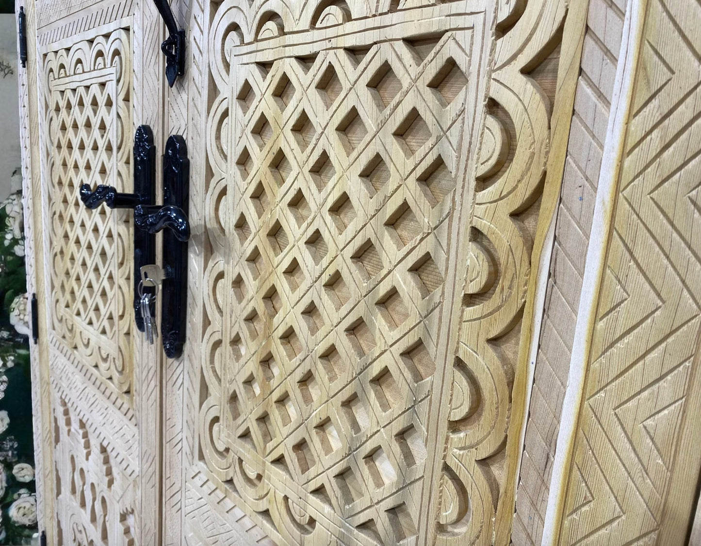 Close-up of a carved wooden door with geometric patterns and black iron hardware.
