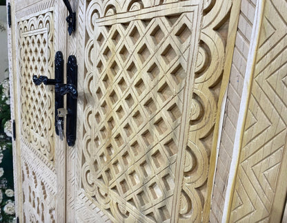 Close-up of a carved wooden door with geometric patterns and black iron hardware.
