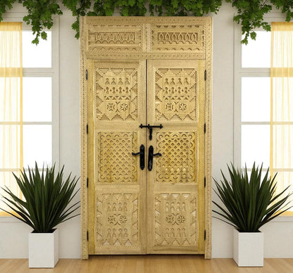 Intricately carved wooden double doors with black hardware, flanked by potted plants under windows.
