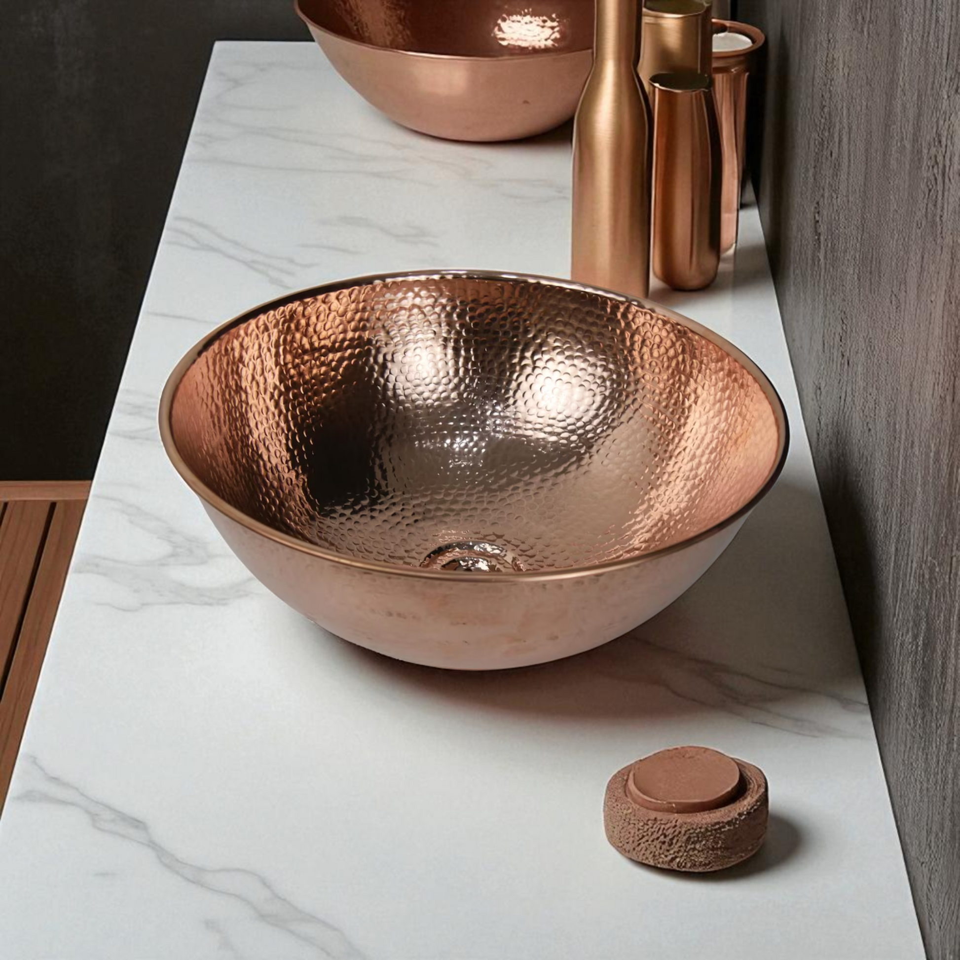 A copper sink on a white marble countertop with copper accessories.