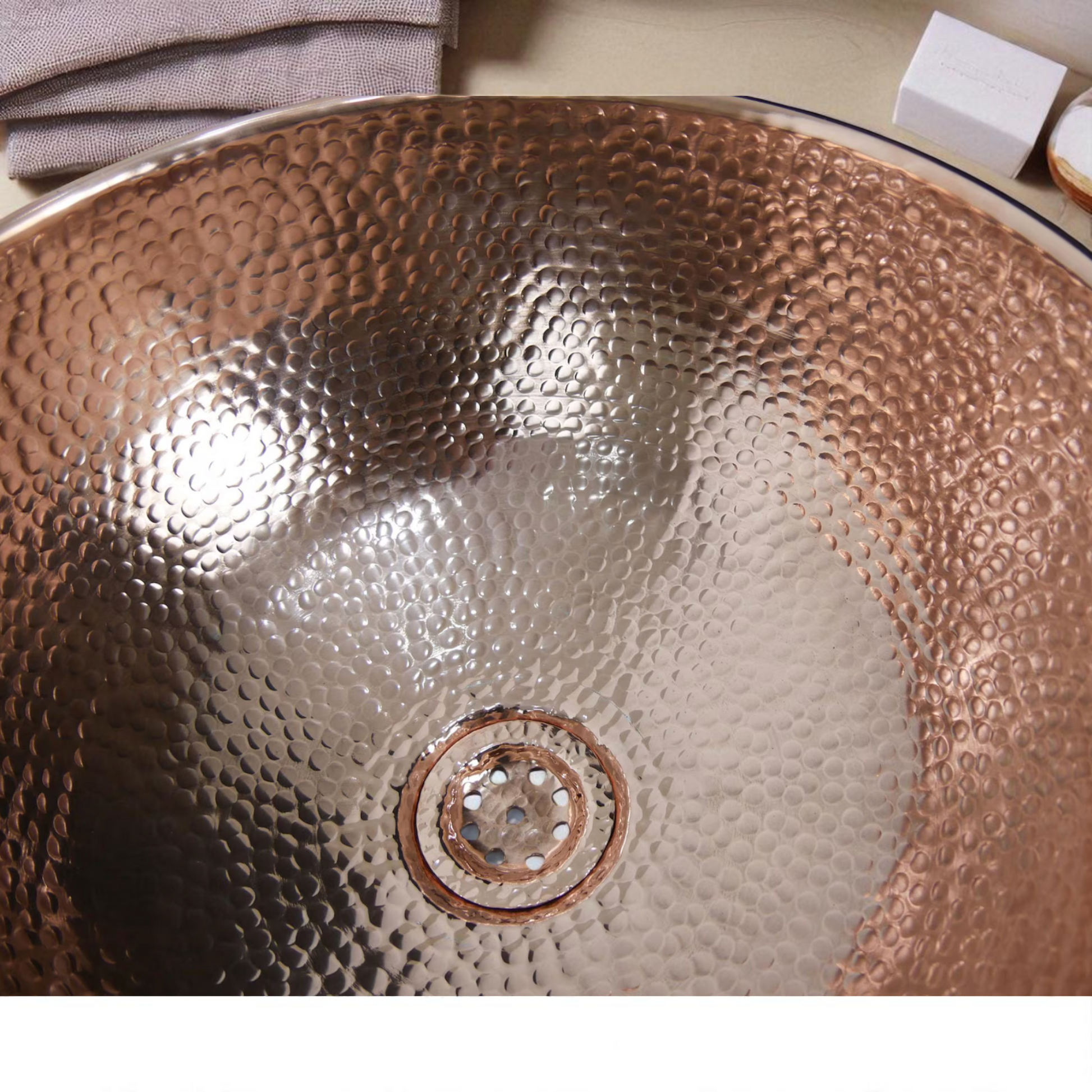 Close-up of a hammered copper sink with a circular drain.