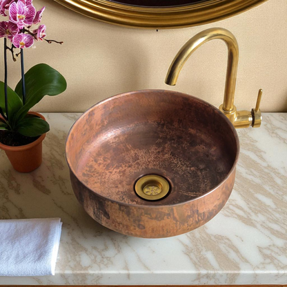 Close-up of a copper sink with a gold faucet, on a marble countertop with a potted orchid and white towel.