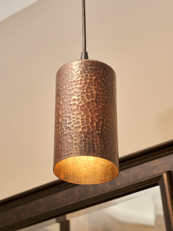 Cylindrical pendant light with a textured surface hanging against a neutral wall.