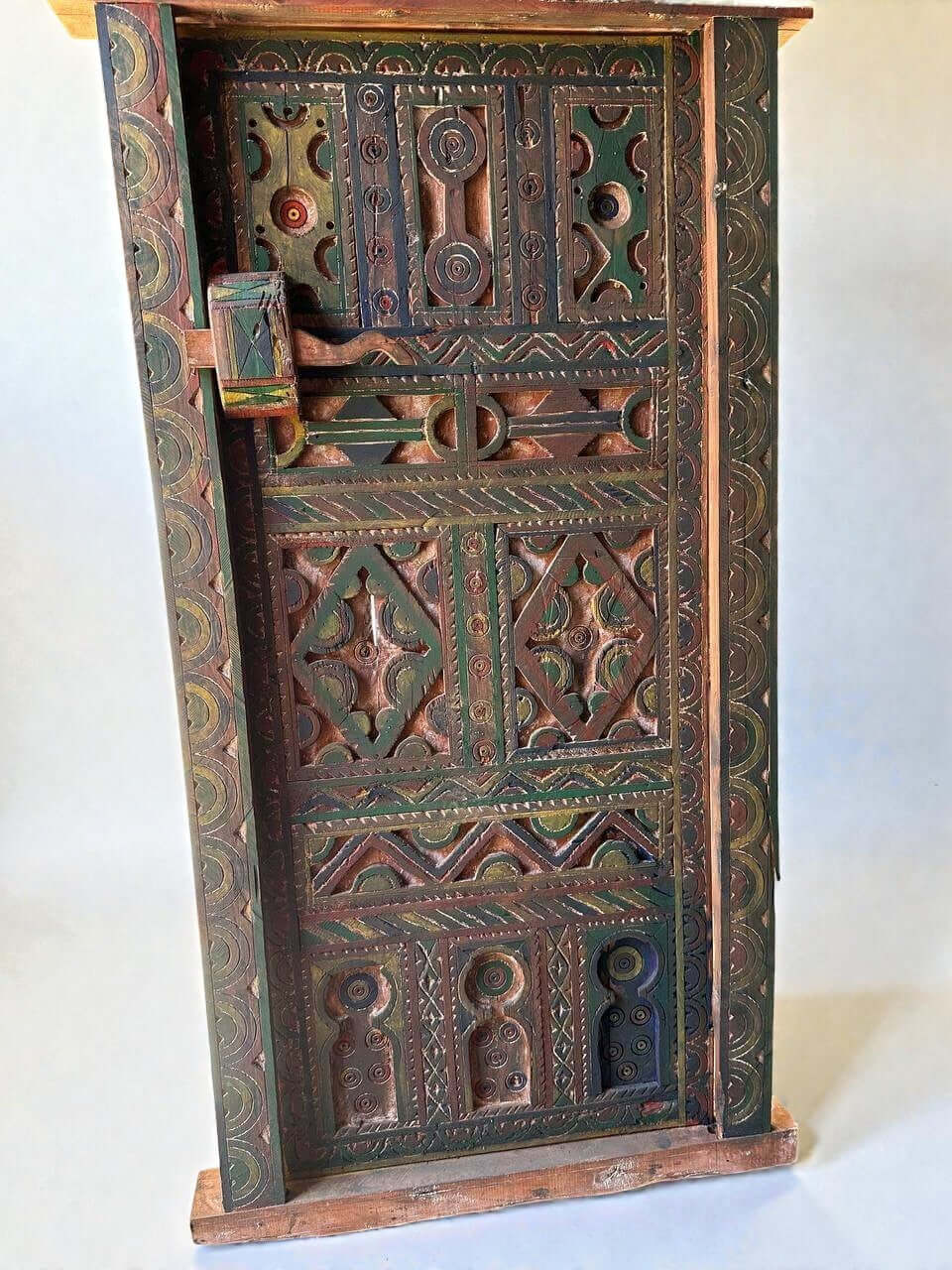 AtlasMuseCrafts handmade wooden door with brass knobs, featuring intricate hand-carved Moroccan geometric patterns in green, red, and brown.