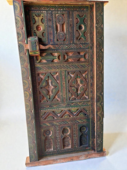 AtlasMuseCrafts handmade wooden door with brass knobs, featuring intricate hand-carved Moroccan geometric patterns in green, red, and brown.