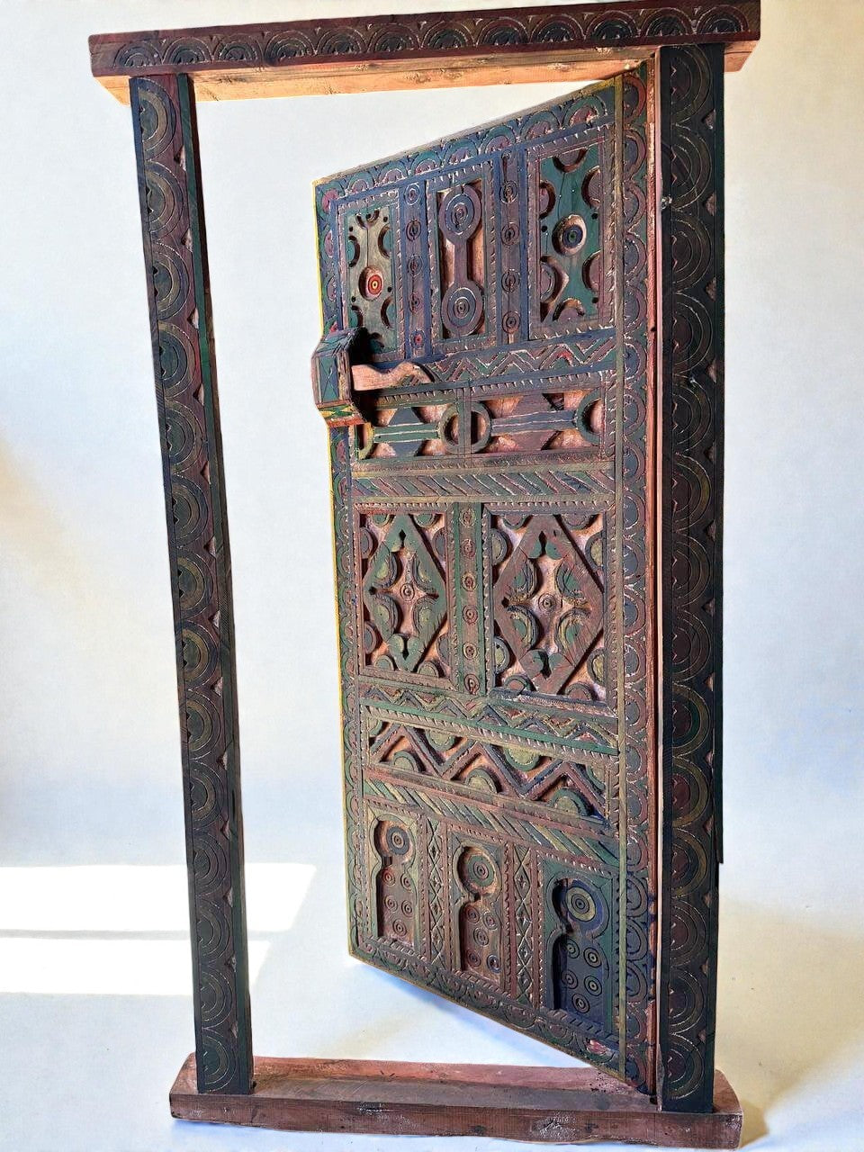 AtlasMuseCrafts handmade wooden door with brass knobs, featuring intricate Moroccan geometric carvings in green, red, and natural wood tones.