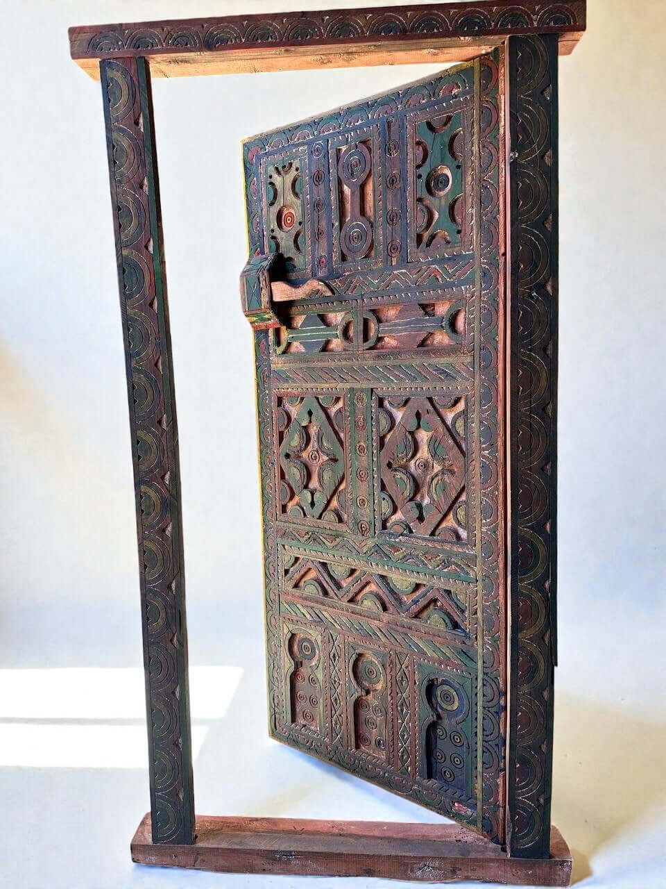 AtlasMuseCrafts handmade wooden door with brass knobs, featuring intricate Moroccan geometric carvings in green, red, and natural wood tones.