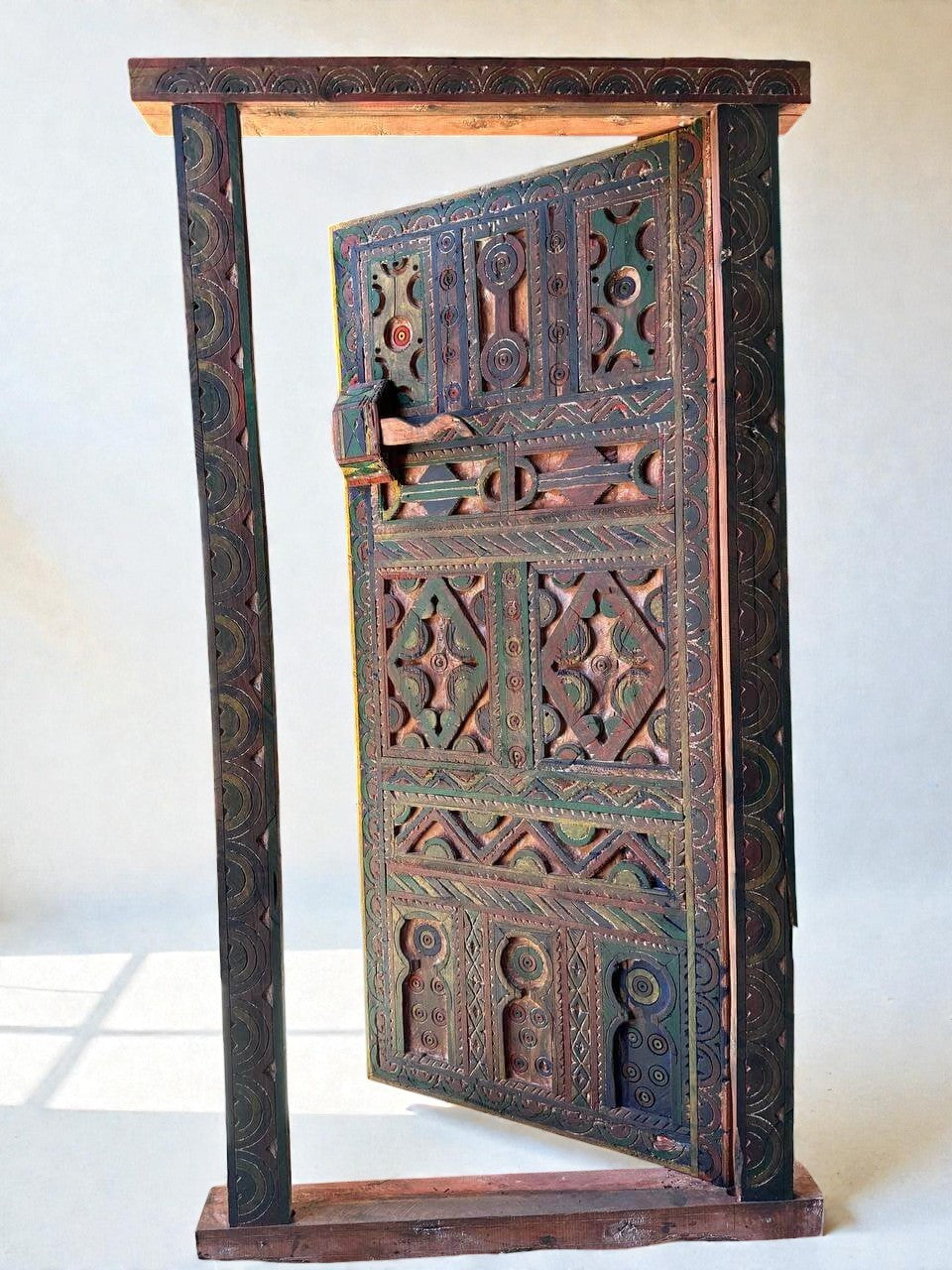 AtlasMuseCrafts handmade wooden door with brass knobs, featuring intricate Moroccan geometric carvings in green, red, and natural wood tones.