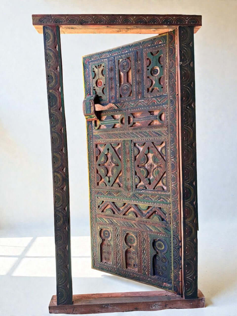 AtlasMuseCrafts handmade wooden door with brass knobs, featuring intricate Moroccan geometric carvings in green, red, and natural wood tones.