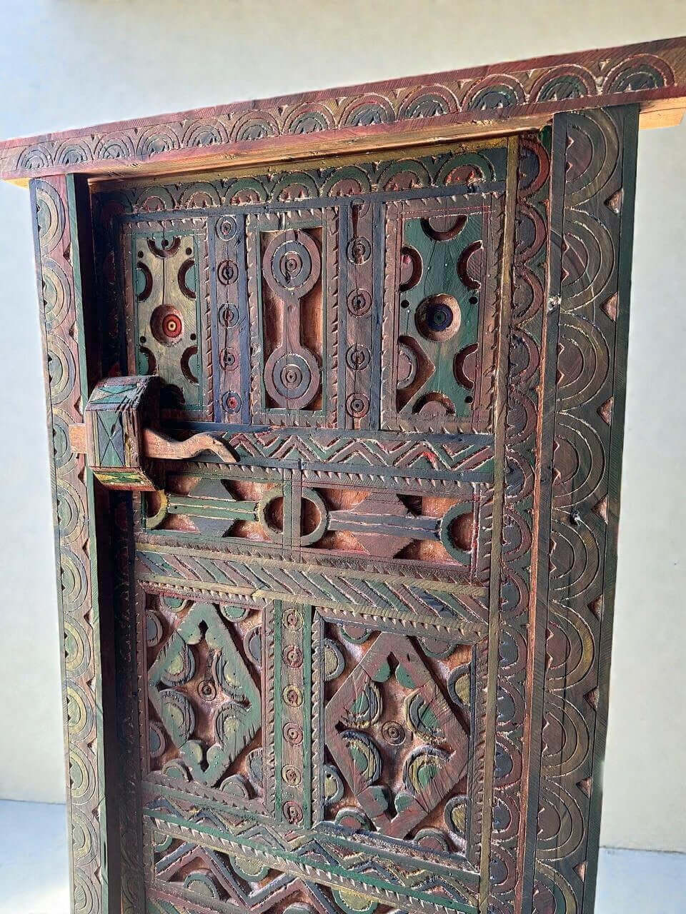 AtlasMuseCrafts handmade wooden door with brass knobs, featuring intricate Moroccan geometric carvings in red, green, and brown wood.