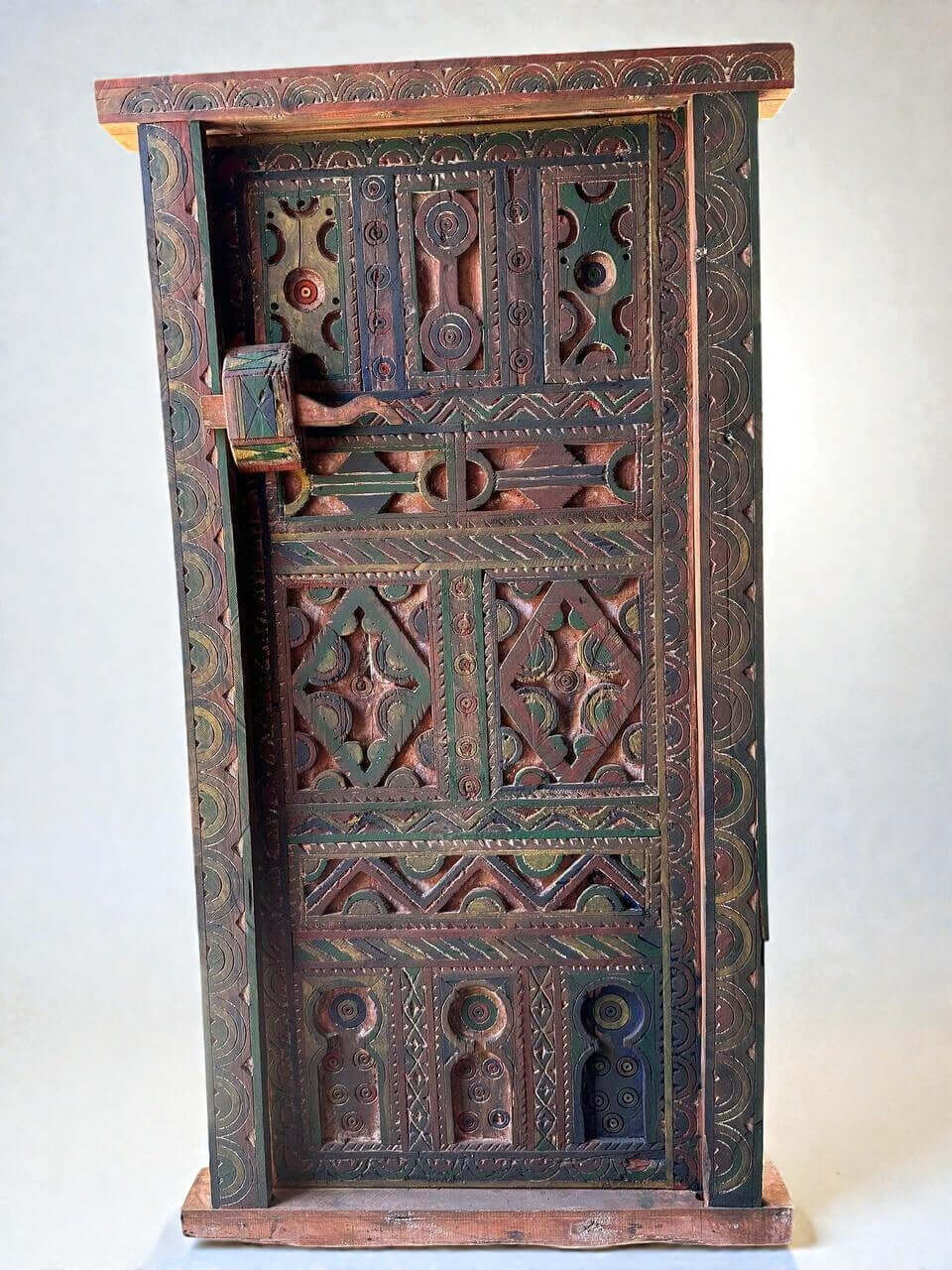 AtlasMuseCrafts handmade wooden door with brass knobs, featuring intricate Moroccan geometric carvings in green, red, and blue.