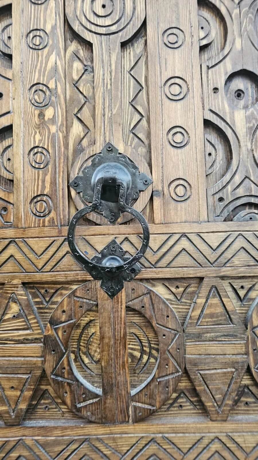 AtlasMuseCrafts antique Moroccan door made of natural wood with intricate Berber carving and a metal ring knocker.