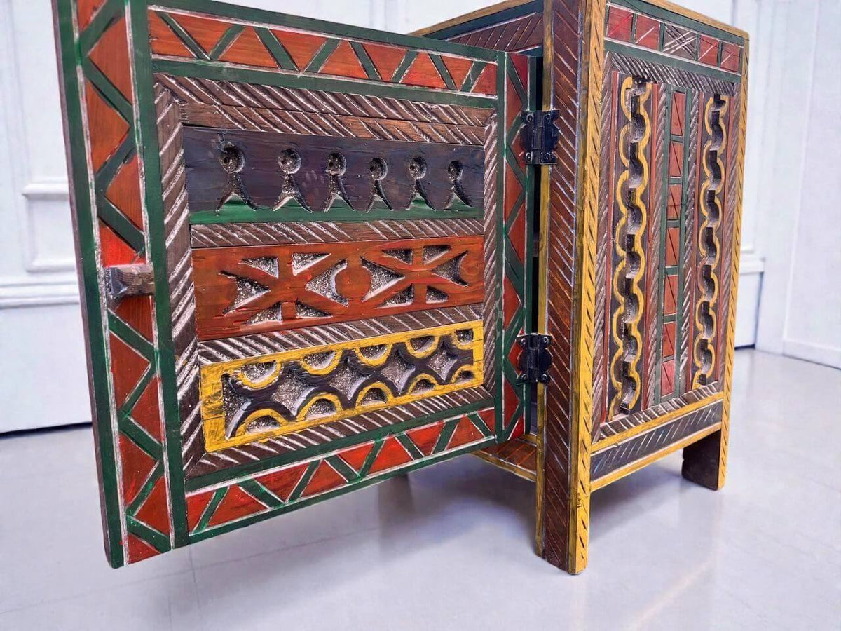 AtlasMuseCrafts handmade wooden cabinet with intricate Berber carvings in red, green, yellow, and brown. Rustic boho style.