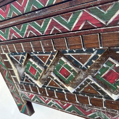 AtlasMuseCrafts handmade wooden cabinet with intricate red, green, and natural wood geometric carvings. Rustic boho style.