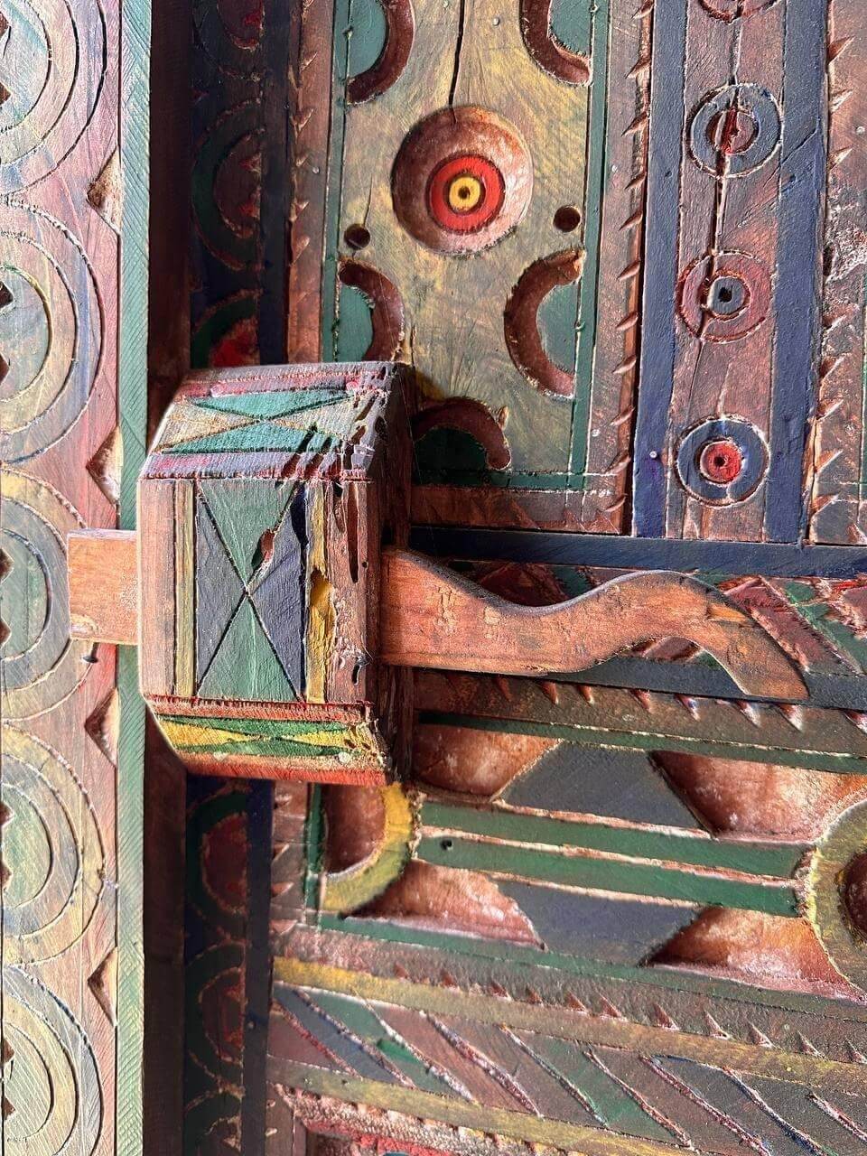 AtlasMuseCrafts handmade wooden door with brass knobs, featuring intricate hand-carved Moroccan geometric patterns in natural wood with painted accents.