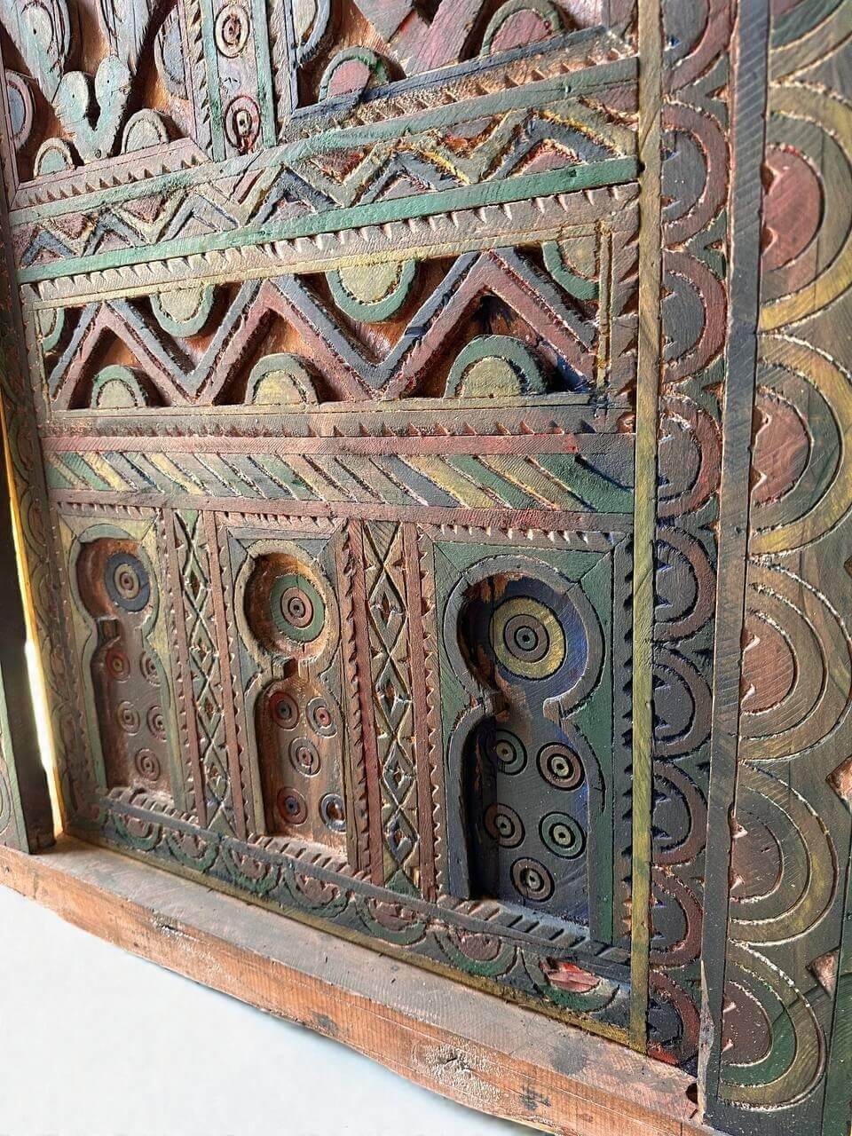 AtlasMuseCrafts handmade wooden door with brass knobs, featuring intricate Moroccan geometric carvings and a distressed multi-color finish.
