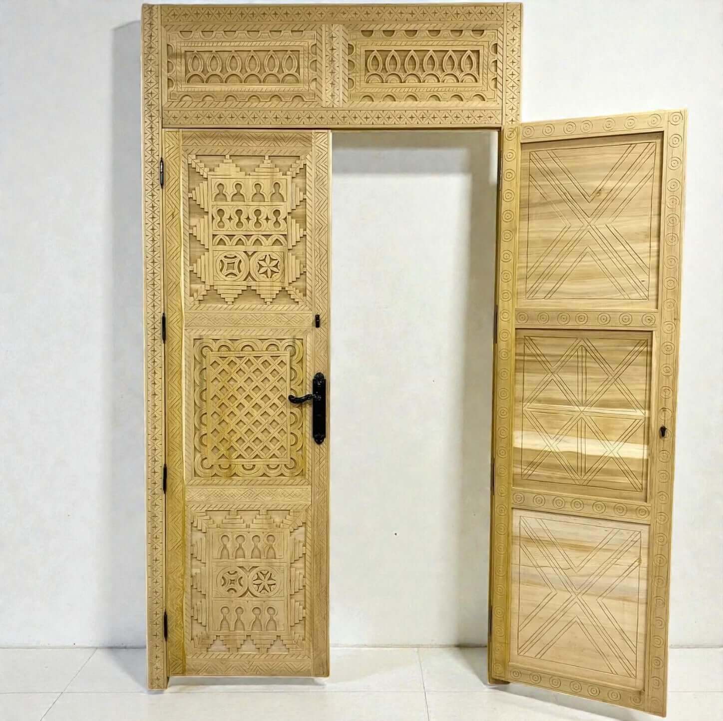 AtlasMuseCrafts handcrafted Moroccan carved wood door with Berber geometric patterns and black hardware. Natural wood.