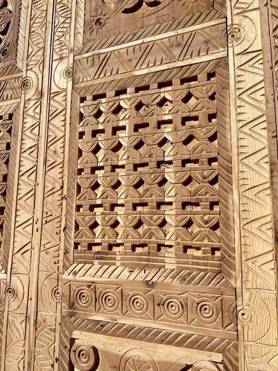 AtlasMuseCrafts antique Moroccan double door with intricate hand-carved geometric and arabesque patterns in natural wood.