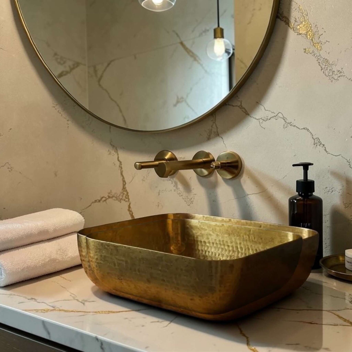 Luxury Hammered Brass Vessel Sink on a marble countertop with towels and a mirror in the background.
