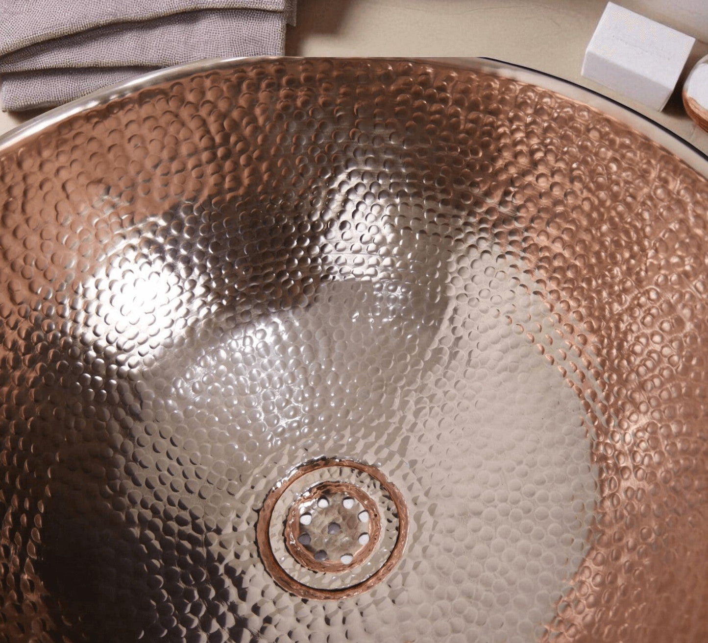 Coppera Studio hammered copper vessel sink with drain. Warm metallic finish and textured surface.