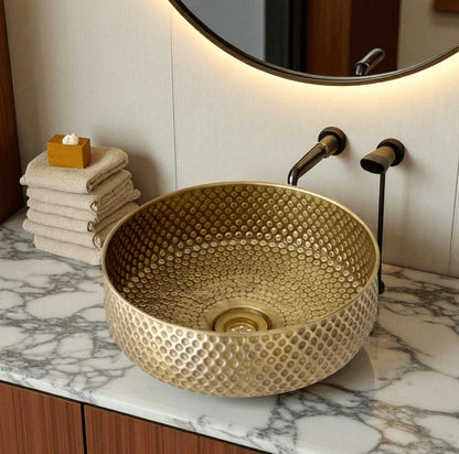 Oxidized copper vessel sink displayed on a marble countertop with modern faucet and neatly folded towels.