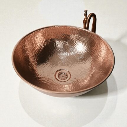Coppera Studio hammered copper vessel sink with a rounded bowl shape and a drain.