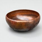 Hammered Brown Copper Vessel Sink displayed on a marble countertop with a lamp and folded towels.