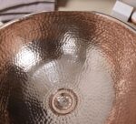 Coppera Studio hammered copper vessel sink with drain. Warm metallic finish and textured surface.