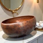 Hammered Brown Copper Vessel Sink placed on a bathroom countertop with a round mirror above.
